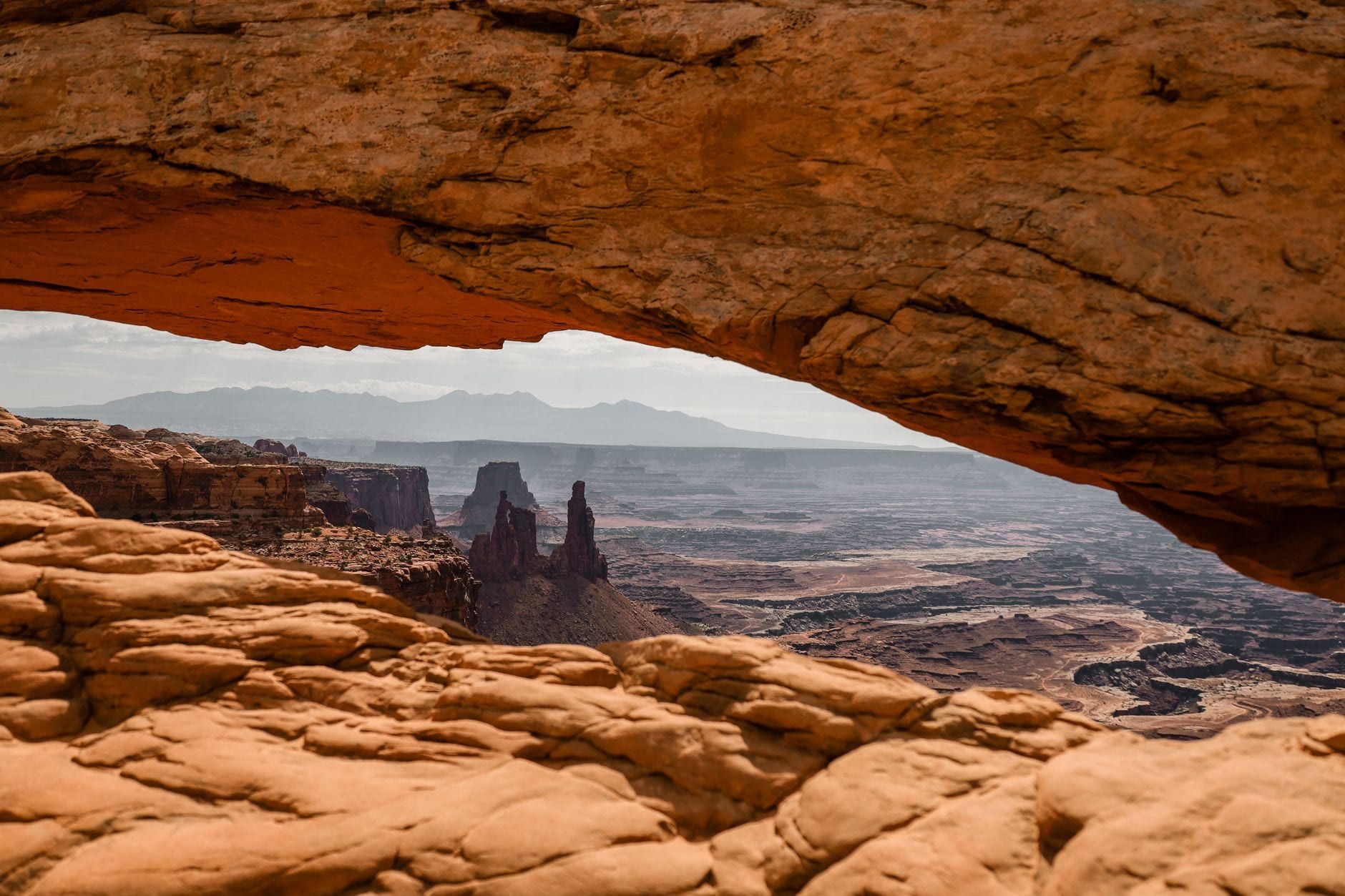 Ein weiter Blick auf tiefe Canyons und entfernte Felstürme, gerahmt unter der natürlichen Steinbrücke des Mesa Arch im Canyonlands-Nationalpark.