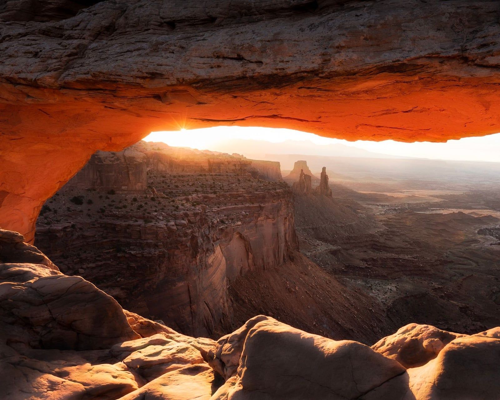 Morning sunlight illuminates the underside of Mesa Arch overlooking the vast canyon landscape in Canyonlands National Park.