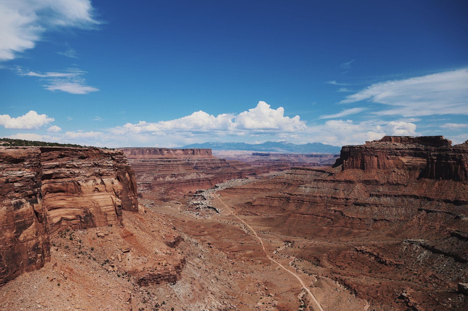 Weite Landschaft mit zerklüfteten roten Felsklippen und der windenden Canyonstraße im Canyonlands-Nationalpark unter leuchtend blauem Himmel.