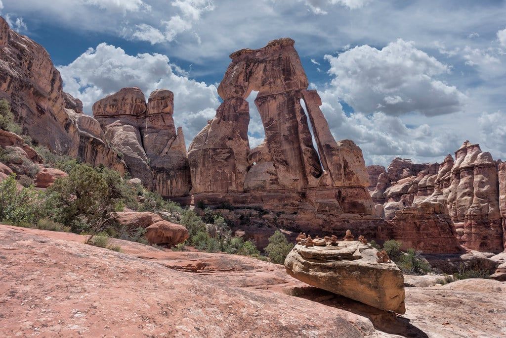 The massive sandstone formation of Druid Arch rises above rocky red terrain under a partly cloudy sky in Canyonlands National Park.