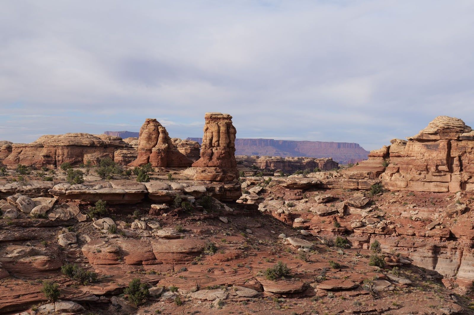 Banded red and buff sandstone spires rise above rugged desert terrain in Canyonlands National Park.