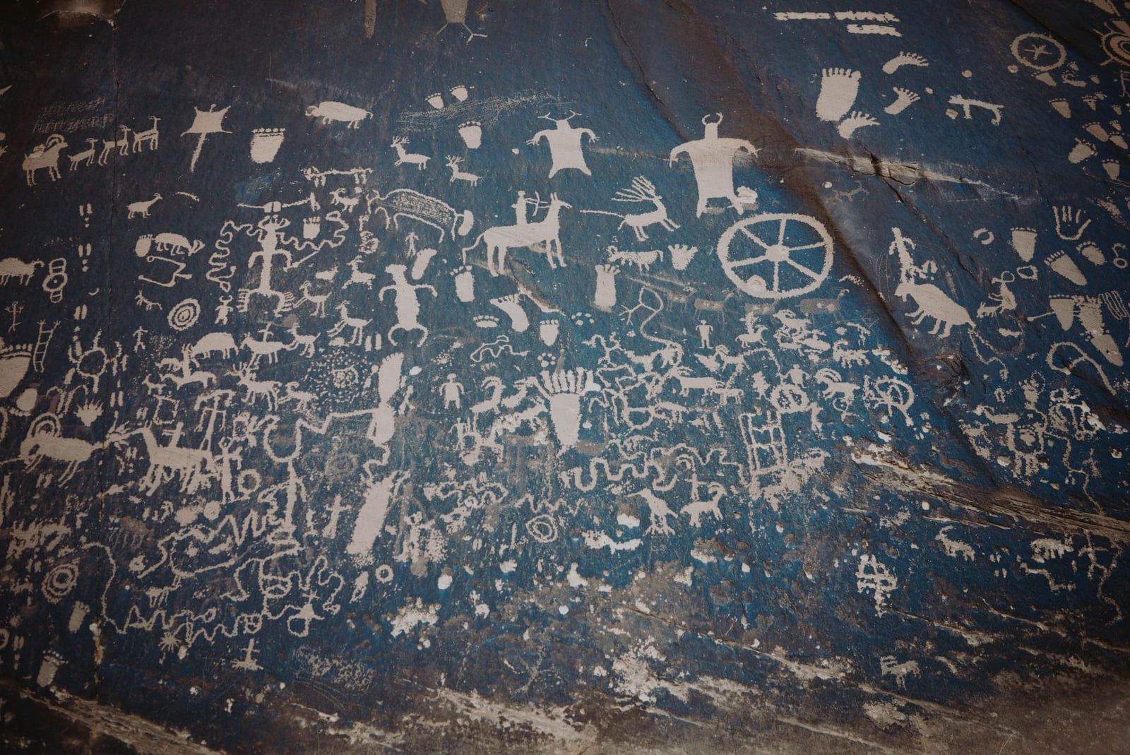 Petroglyphs depicting animals, human figures, and symbols carved into a desert varnish rock face at Newspaper Rock near Canyonlands National Park.