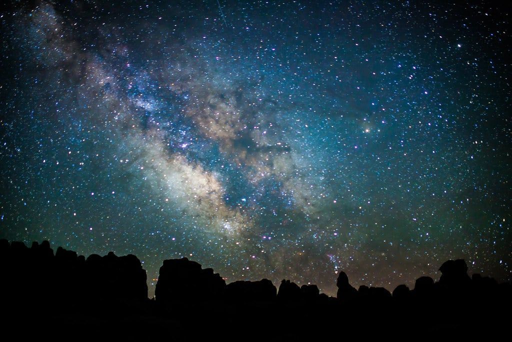 The Milky Way shines brightly in the night sky above rock spires in Canyonlands National Park.